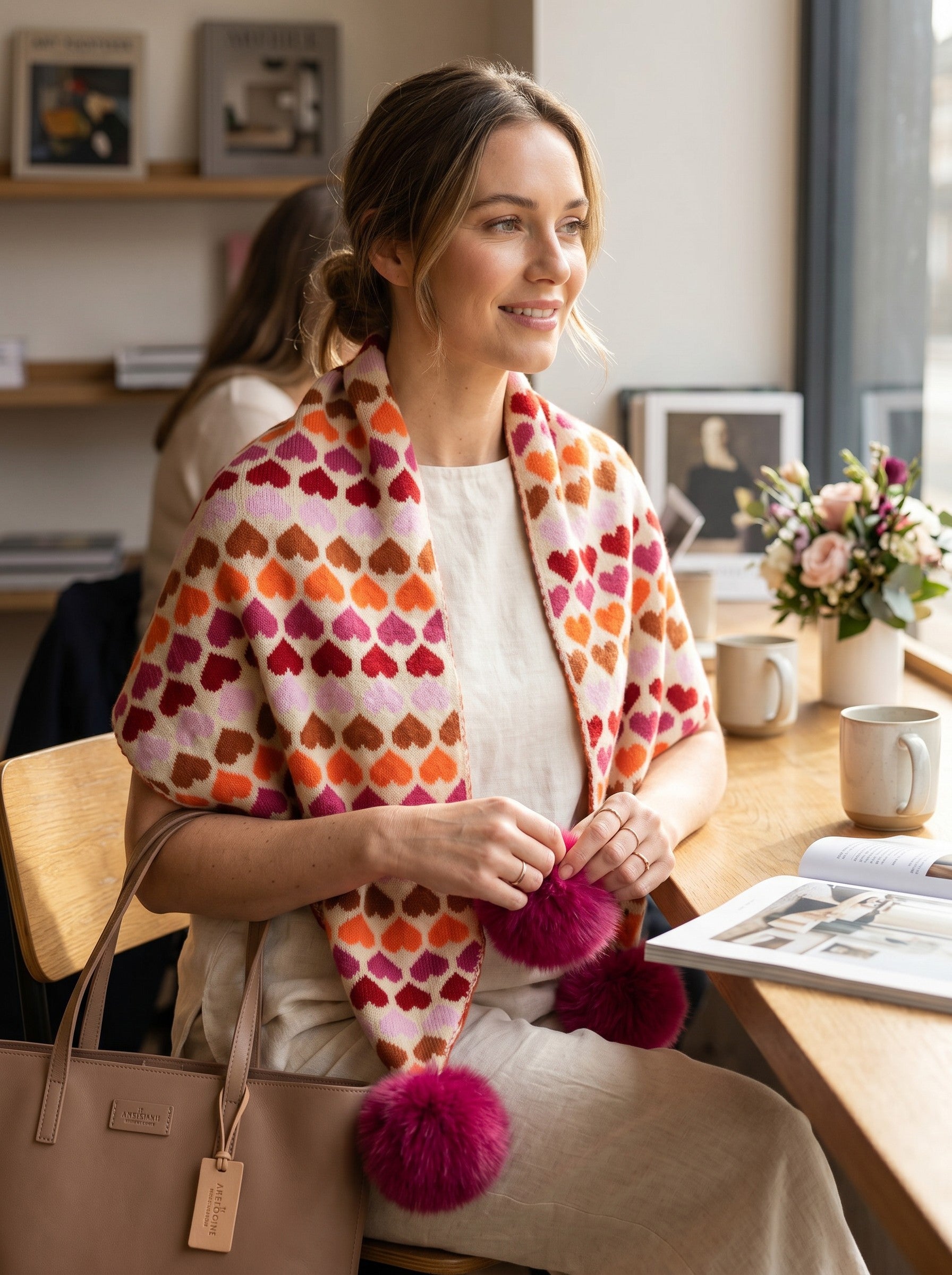 Color's Wholesale heart-patterned knit shawl in orange, pink, and cream with large fuchsia pom-pom accents.