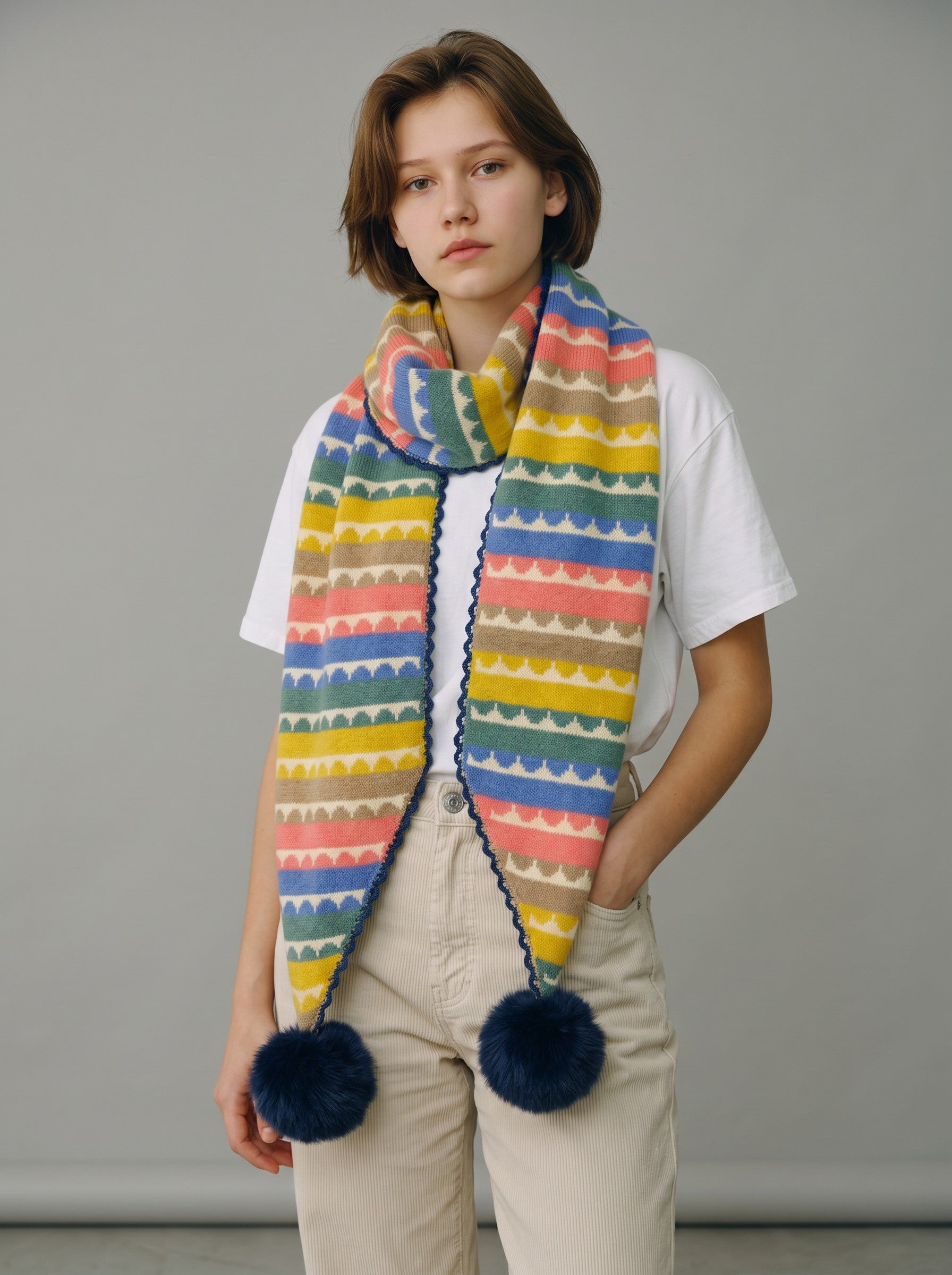 Color's Wholesale multi-colored striped knit scarf with scalloped patterns and navy blue pom-poms on ends