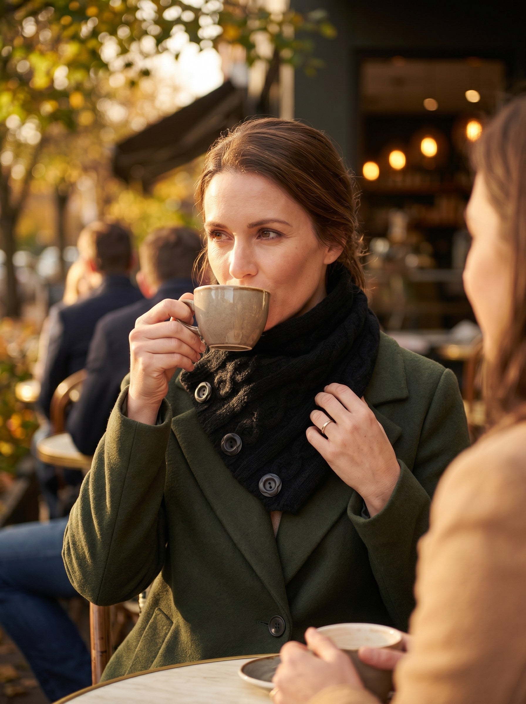 Woman wearing a black Color's Wholesale cable-knit button scarf with an olive green coat at an outdoor cafe