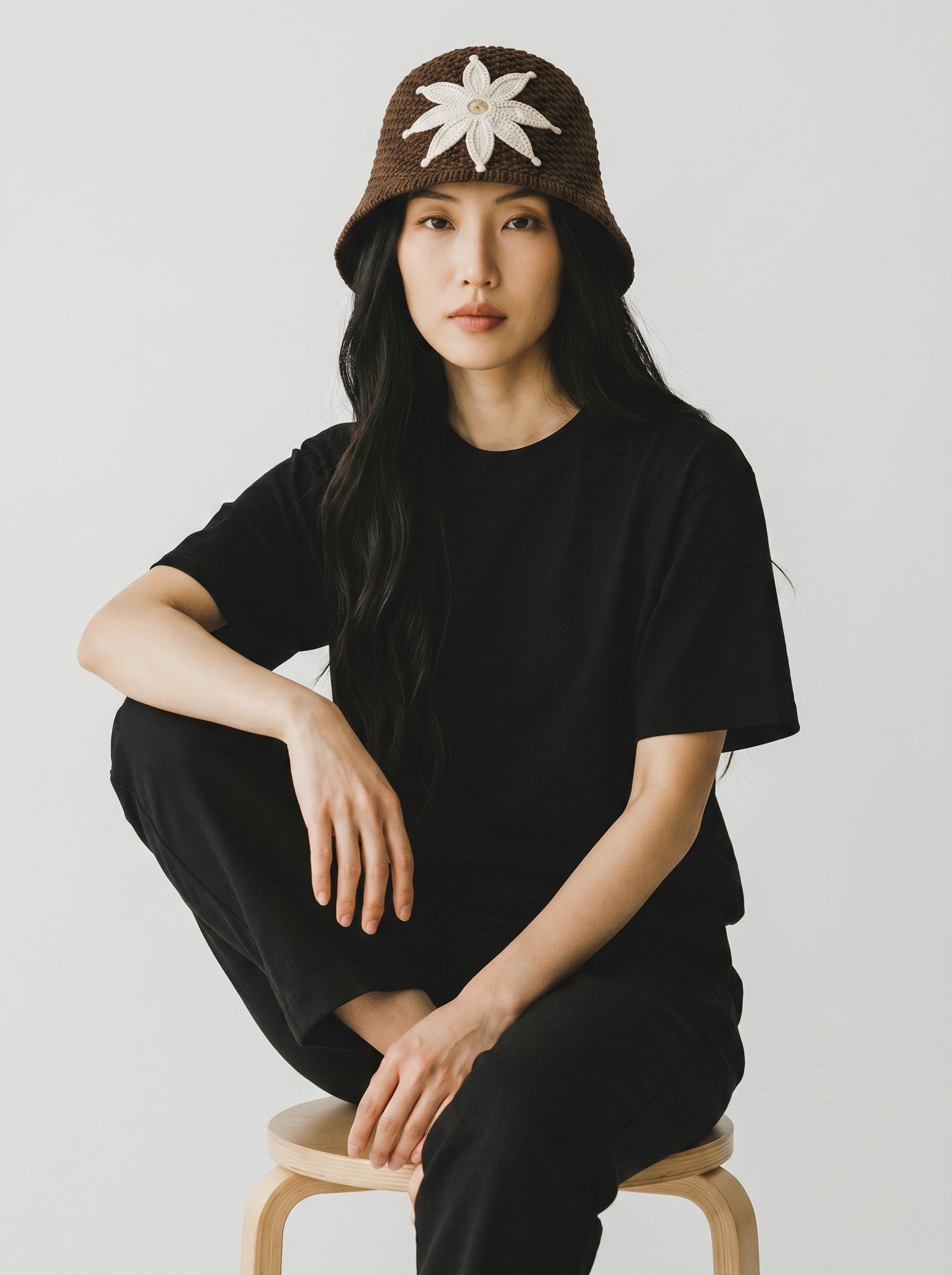 Color's Wholesale brown crocheted bucket hat with cream flower appliqué and button detail.