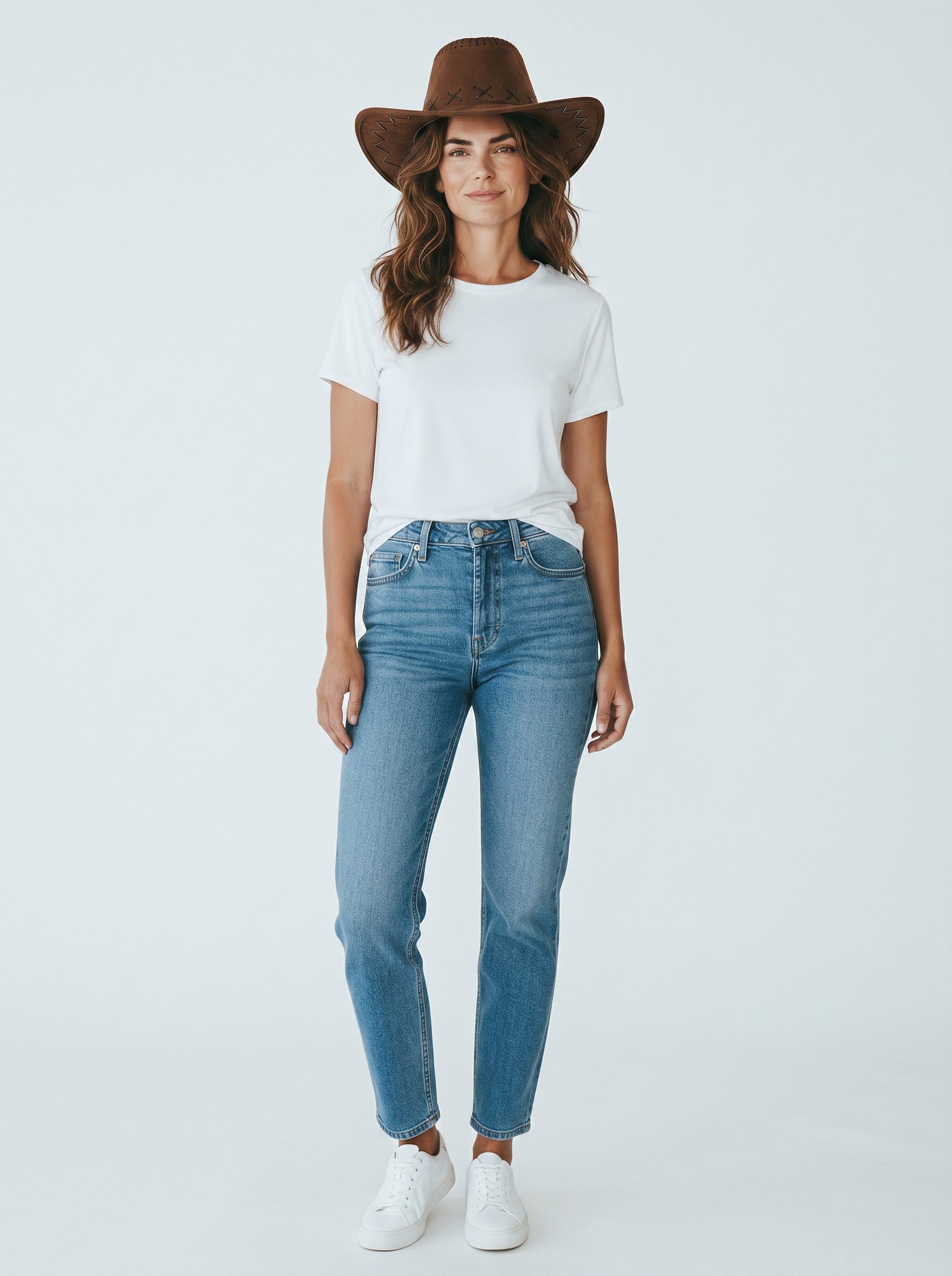 Woman wearing a brown Color's Wholesale faux leather cowboy hat with stitched detailing, white t-shirt, and jeans.