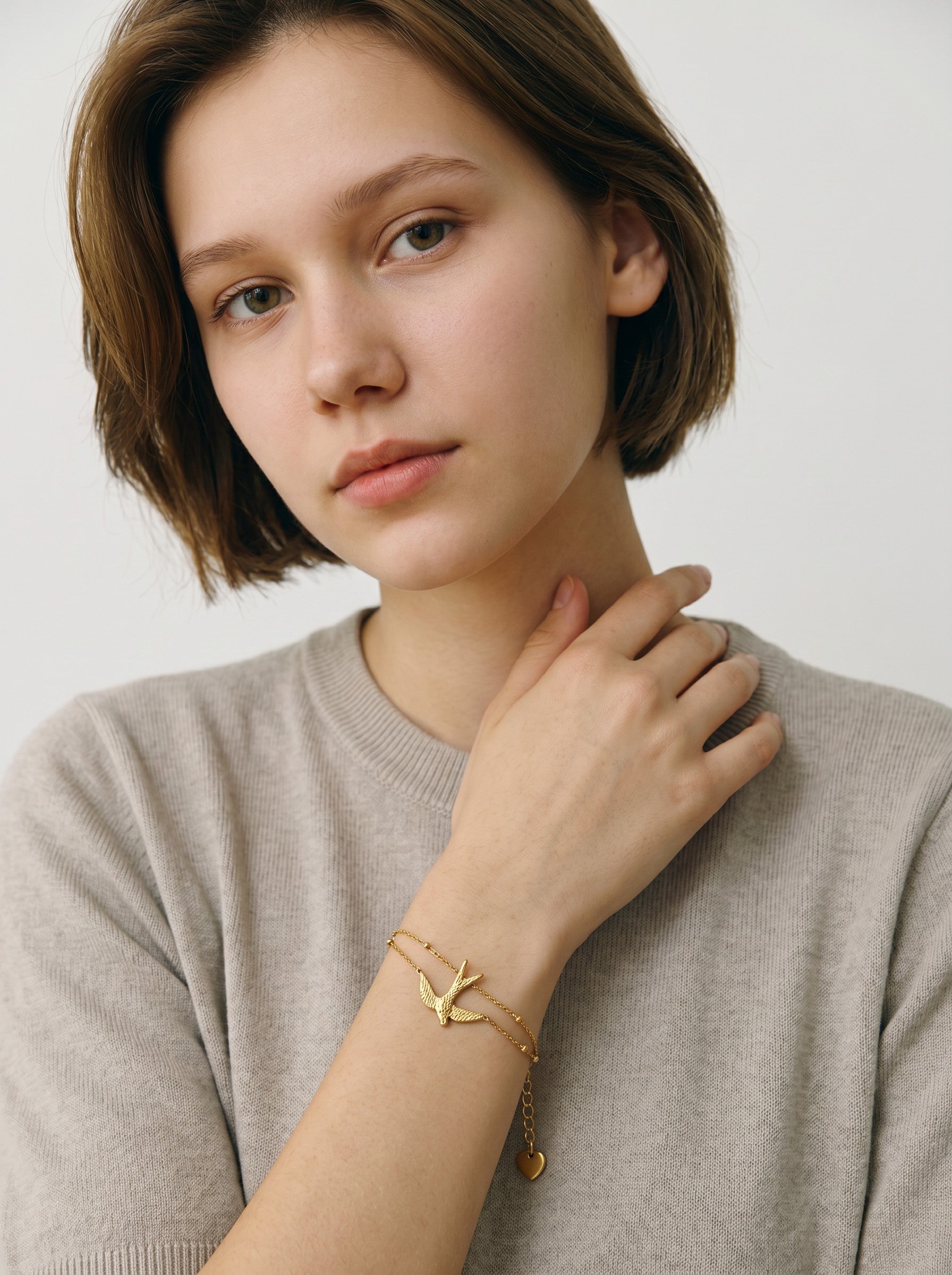 Color's Wholesale gold-tone double chain bracelet with a bird charm worn by a woman in a beige sweater.