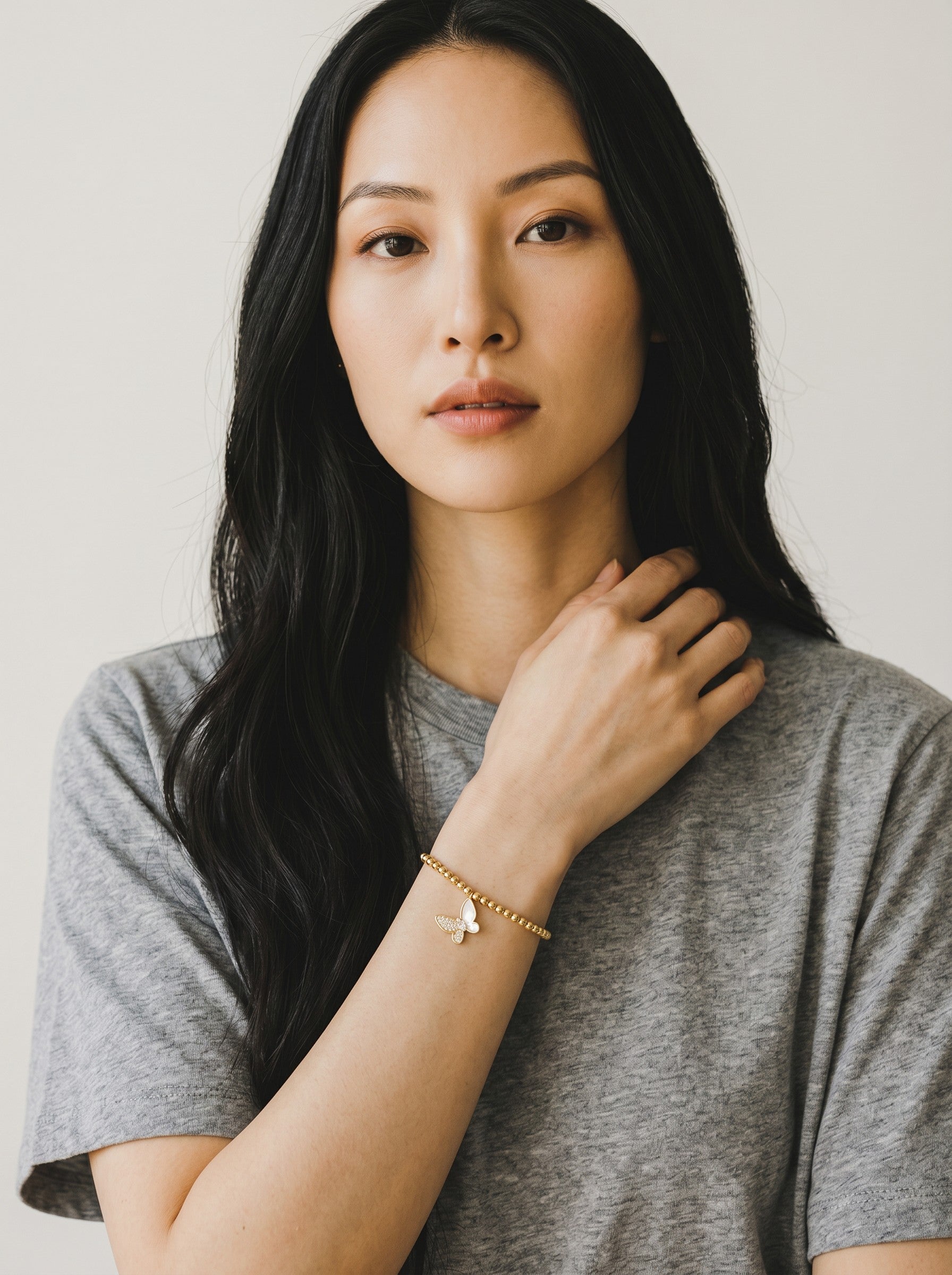 Color's Wholesale gold beaded bracelet with a sparkling butterfly charm worn by a woman in a grey t-shirt.