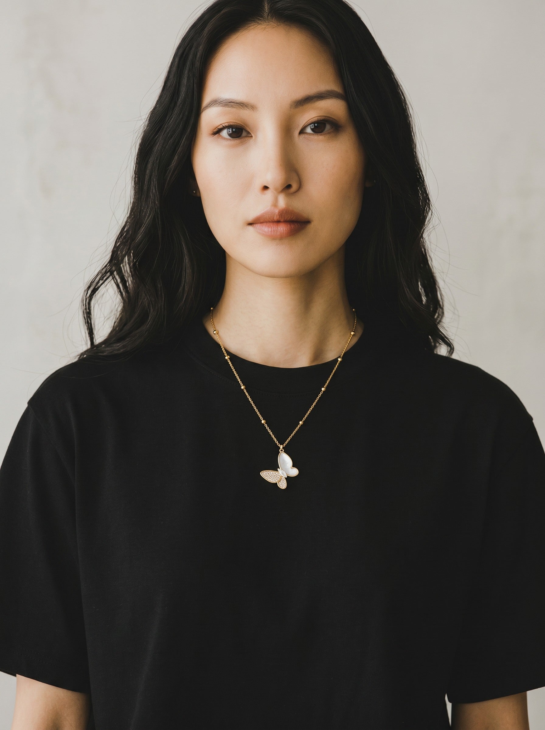Color's Wholesale gold chain necklace featuring a delicate white butterfly pendant worn by a woman in a black shirt