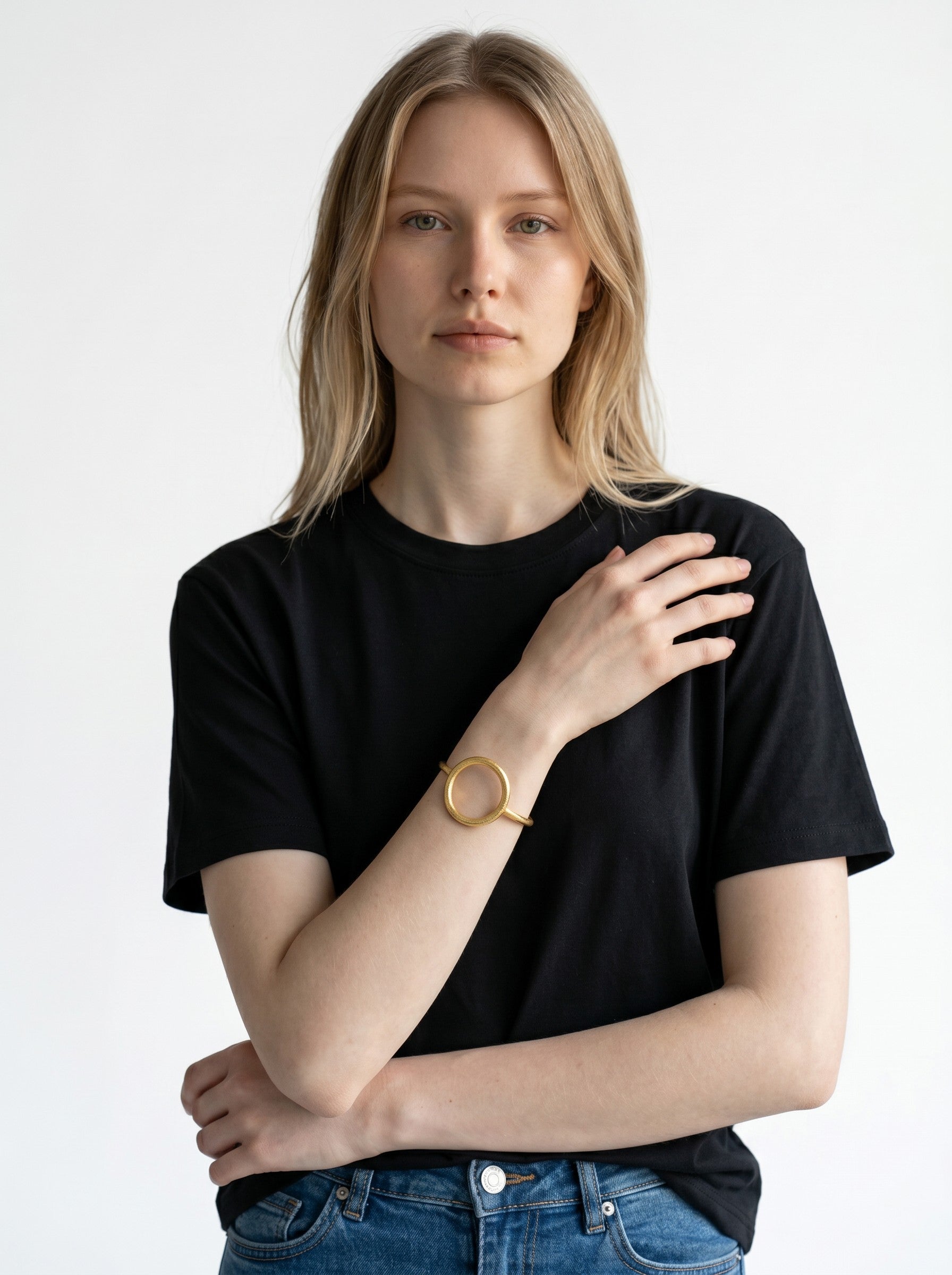 Color's Wholesale gold-tone circular bangle bracelet worn on the wrist of a woman in a black t-shirt