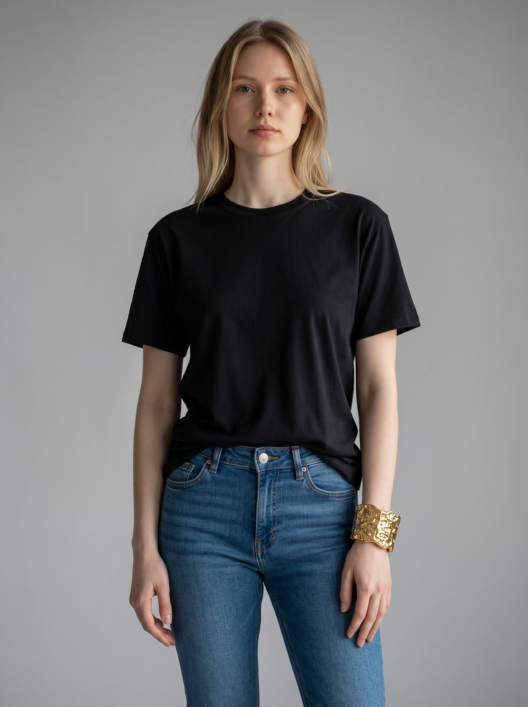 Color's Wholesale model wearing a black t-shirt, blue jeans, and a wide textured gold cuff bracelet