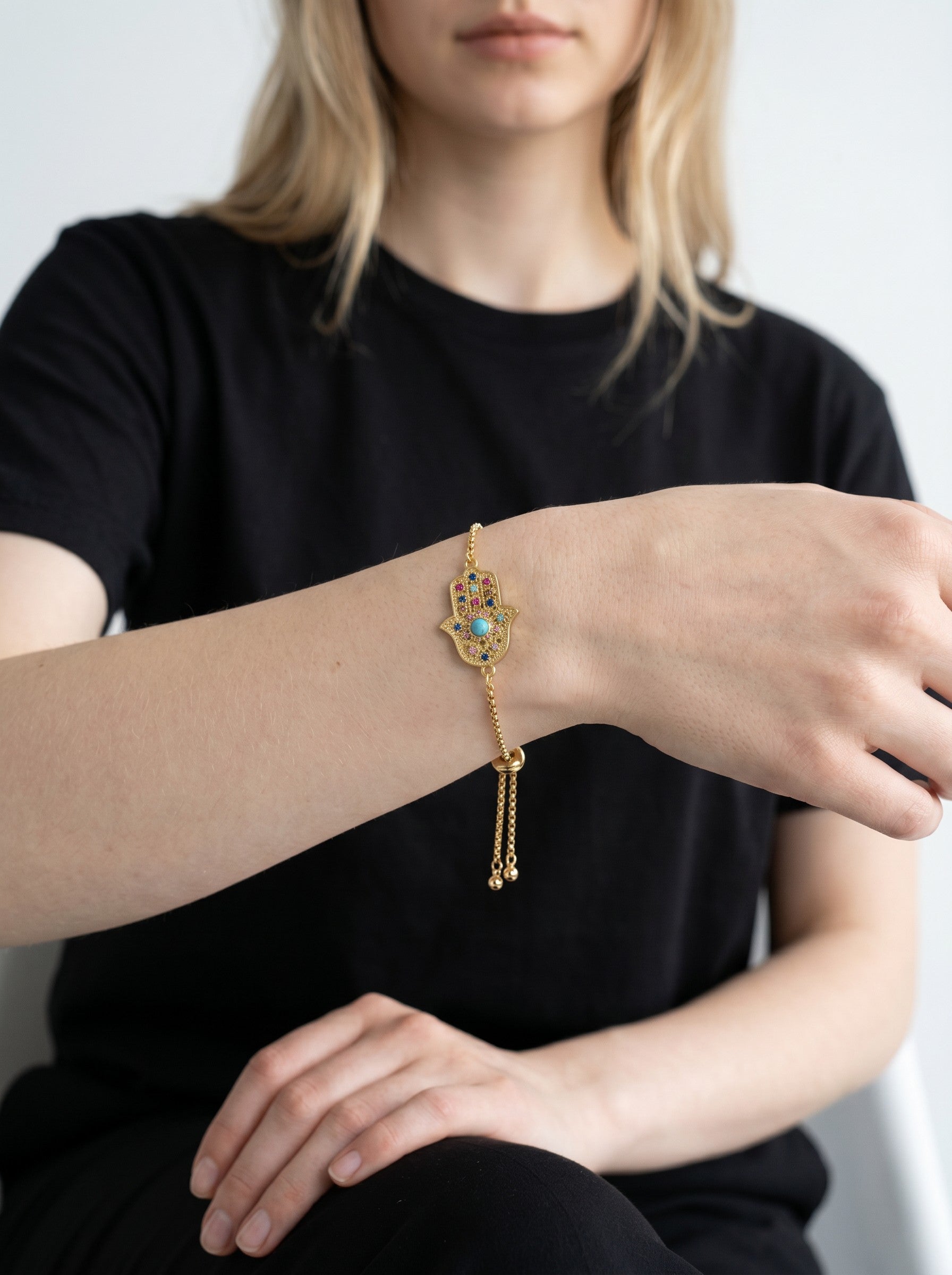 Color's Wholesale gold hamsa hand bracelet with colorful stones and turquoise center worn on a woman's wrist