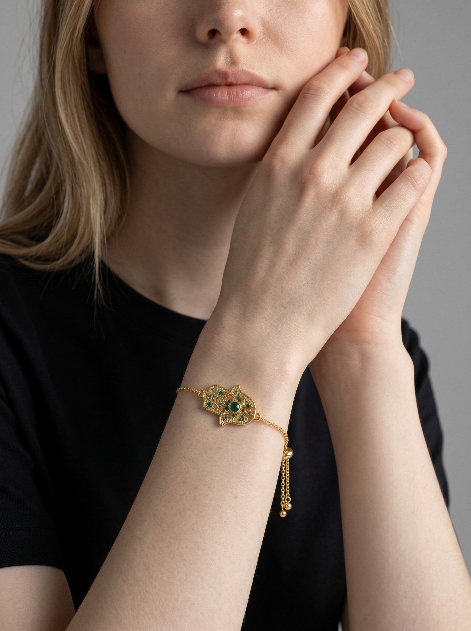 Color's Wholesale gold hamsa hand bracelet with green and orange stones worn on a woman's wrist