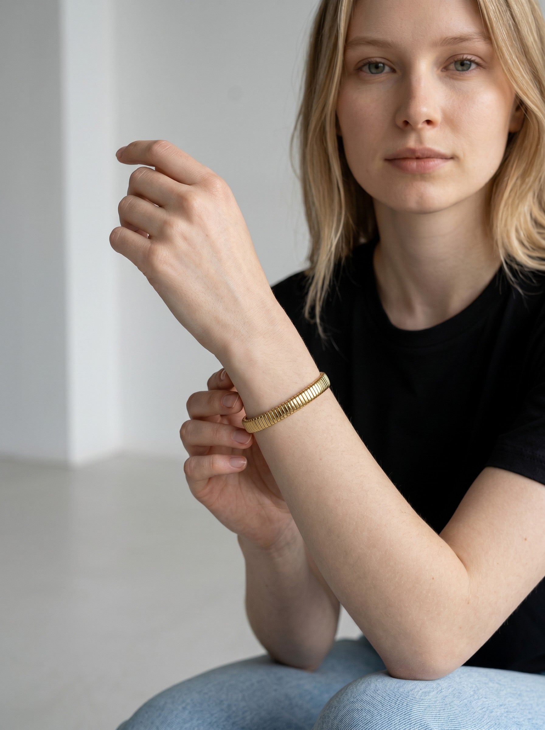 Color's Wholesale gold-toned flexible link bracelet worn on a model's wrist with a black t-shirt