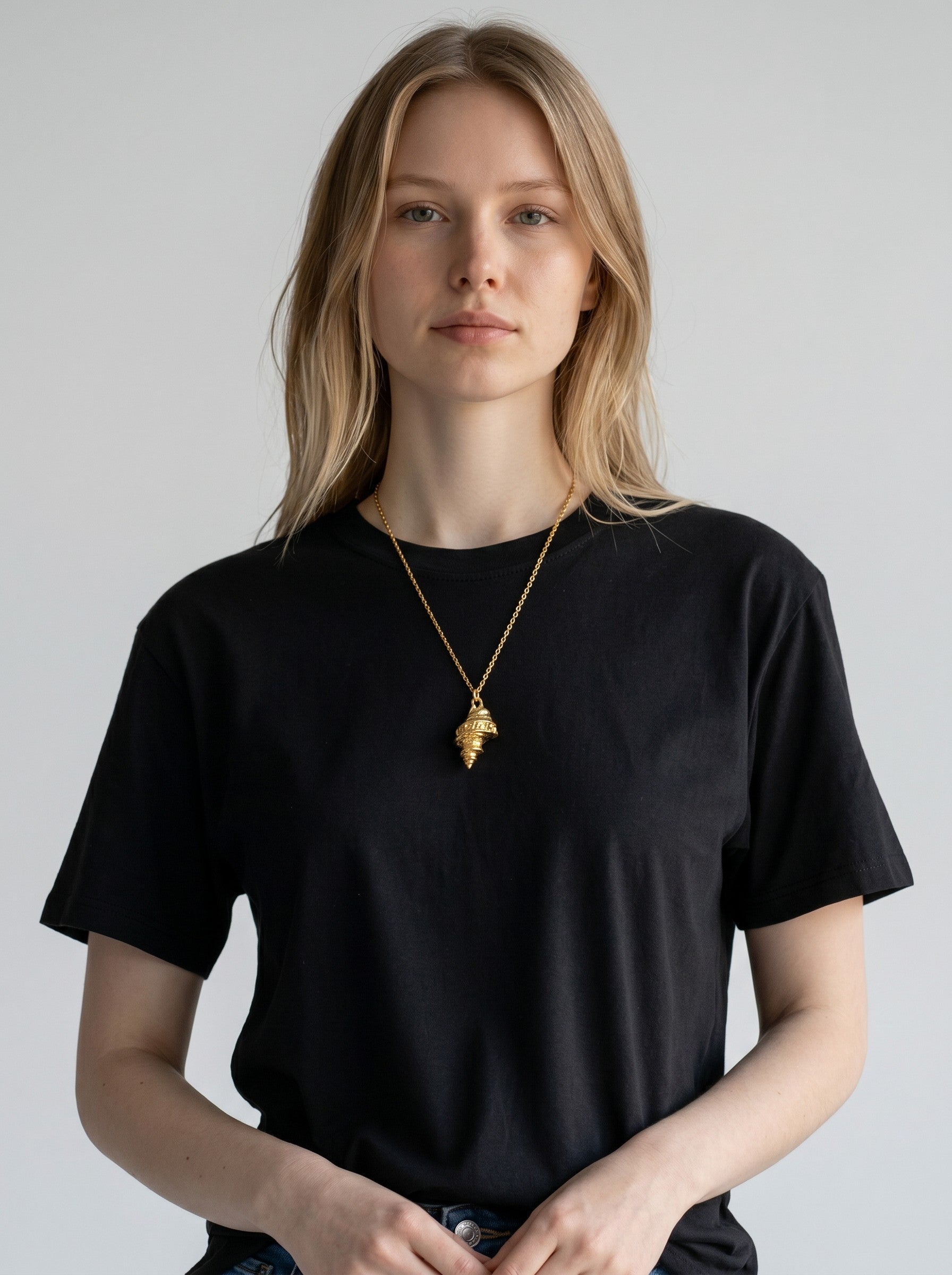 Model wearing a Color's Wholesale gold seashell pendant necklace with a black t-shirt against a neutral background