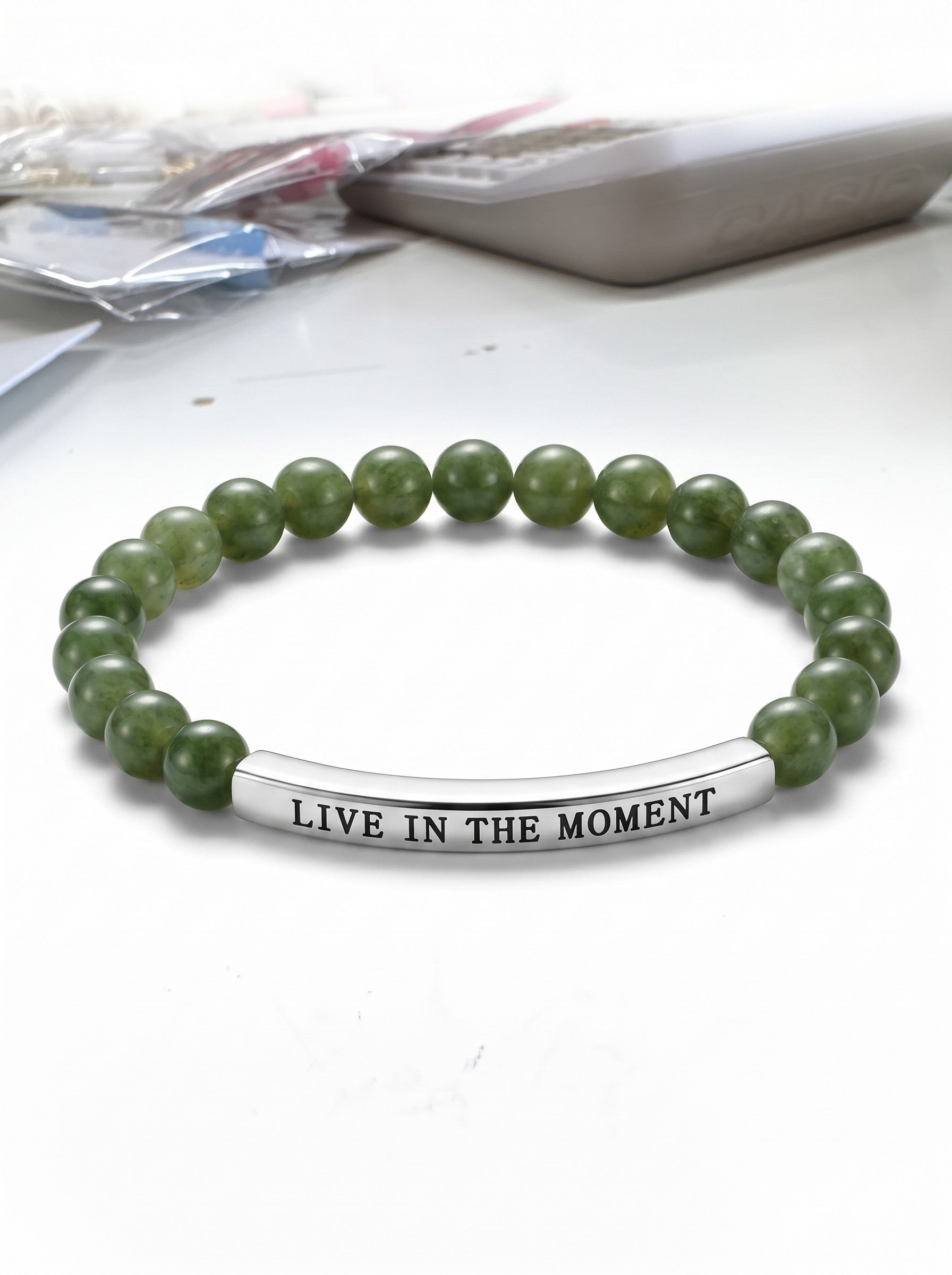 Color's Wholesale green beaded stretch bracelet featuring a silver bar charm engraved with Live in the Moment text.