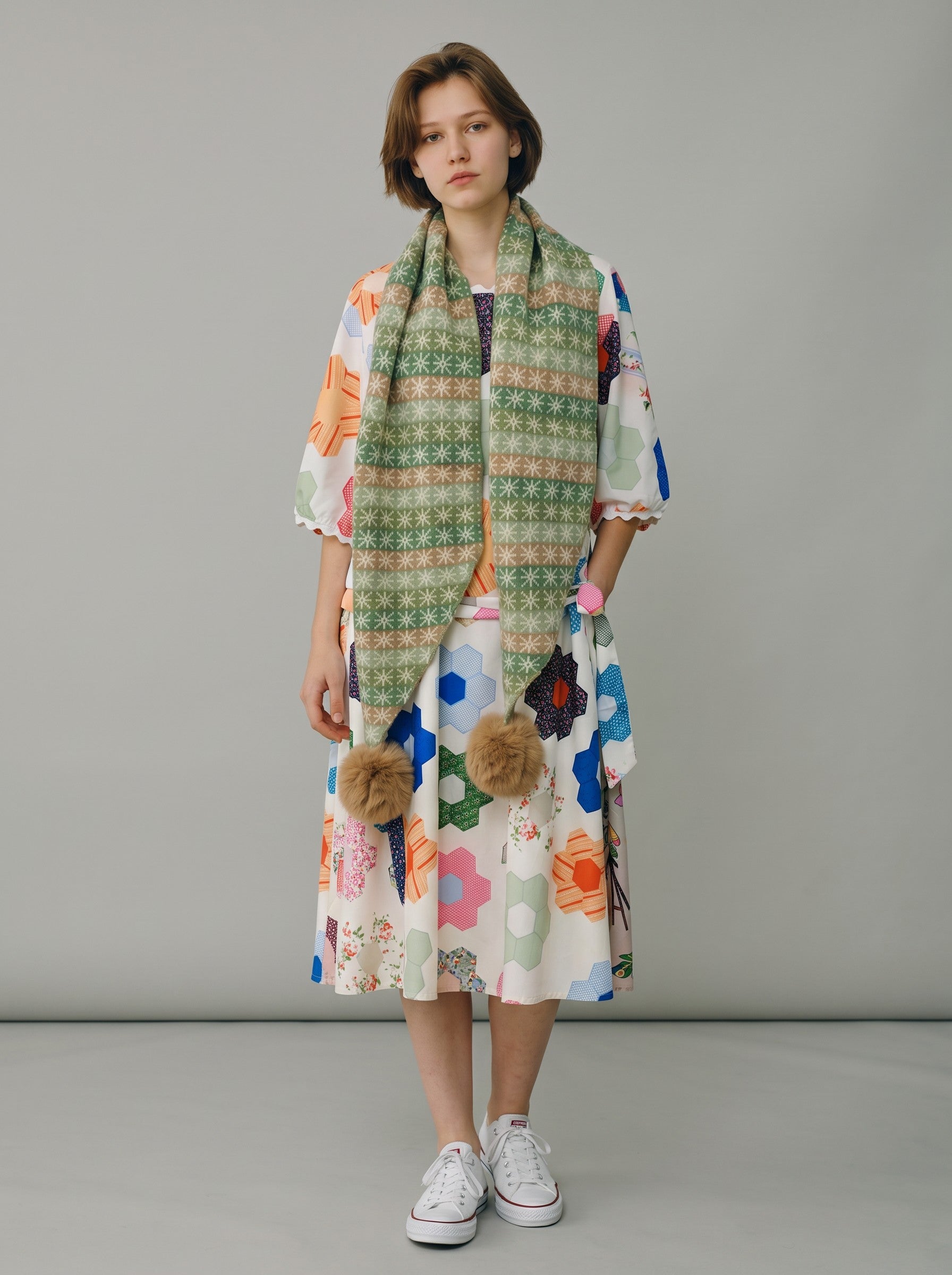 Color's Wholesale green patterned scarf with pom-poms worn by a model in a colorful geometric print dress