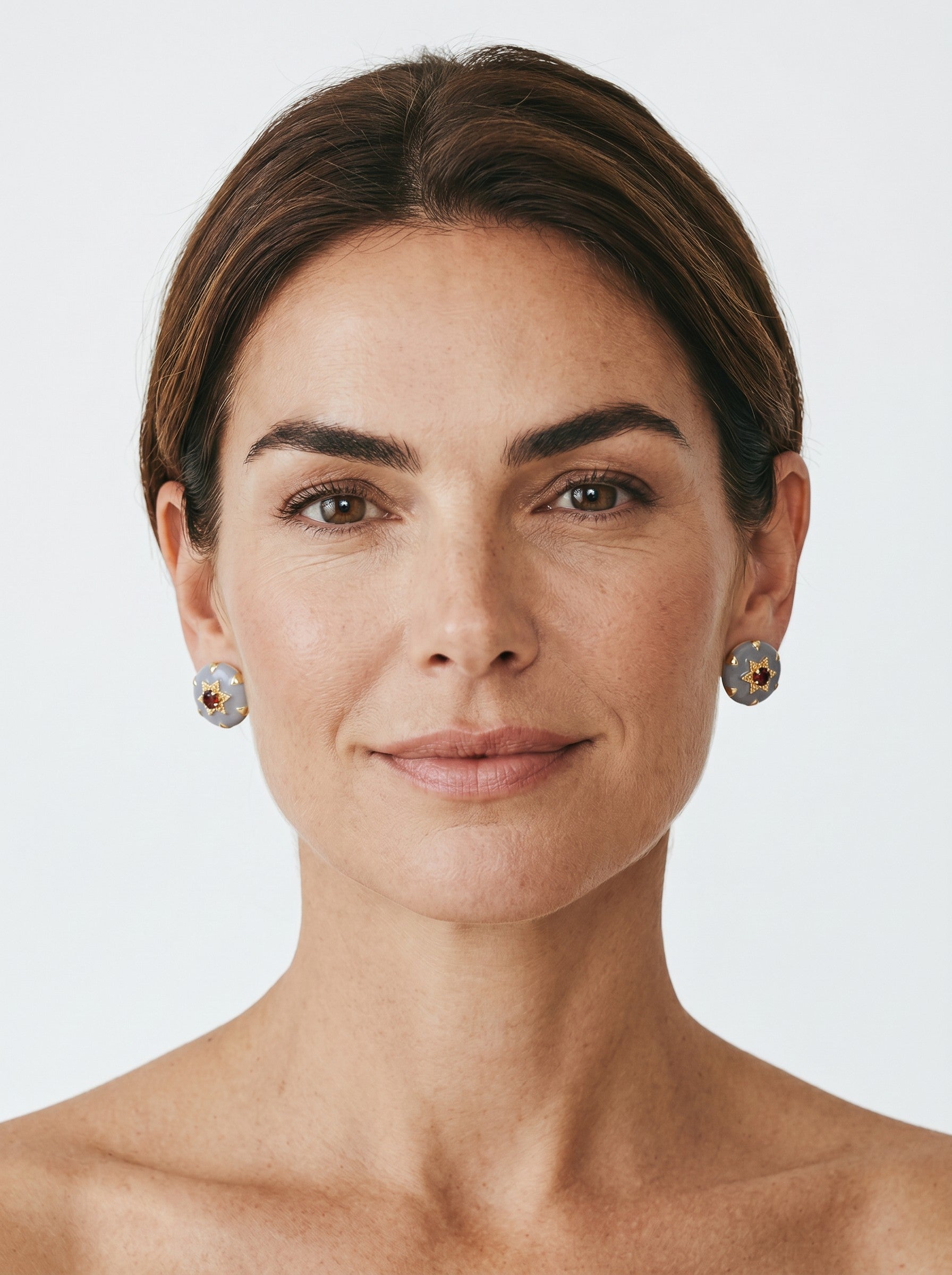 Color's Wholesale grey stud earrings with gold star accents and central red stones worn by a woman