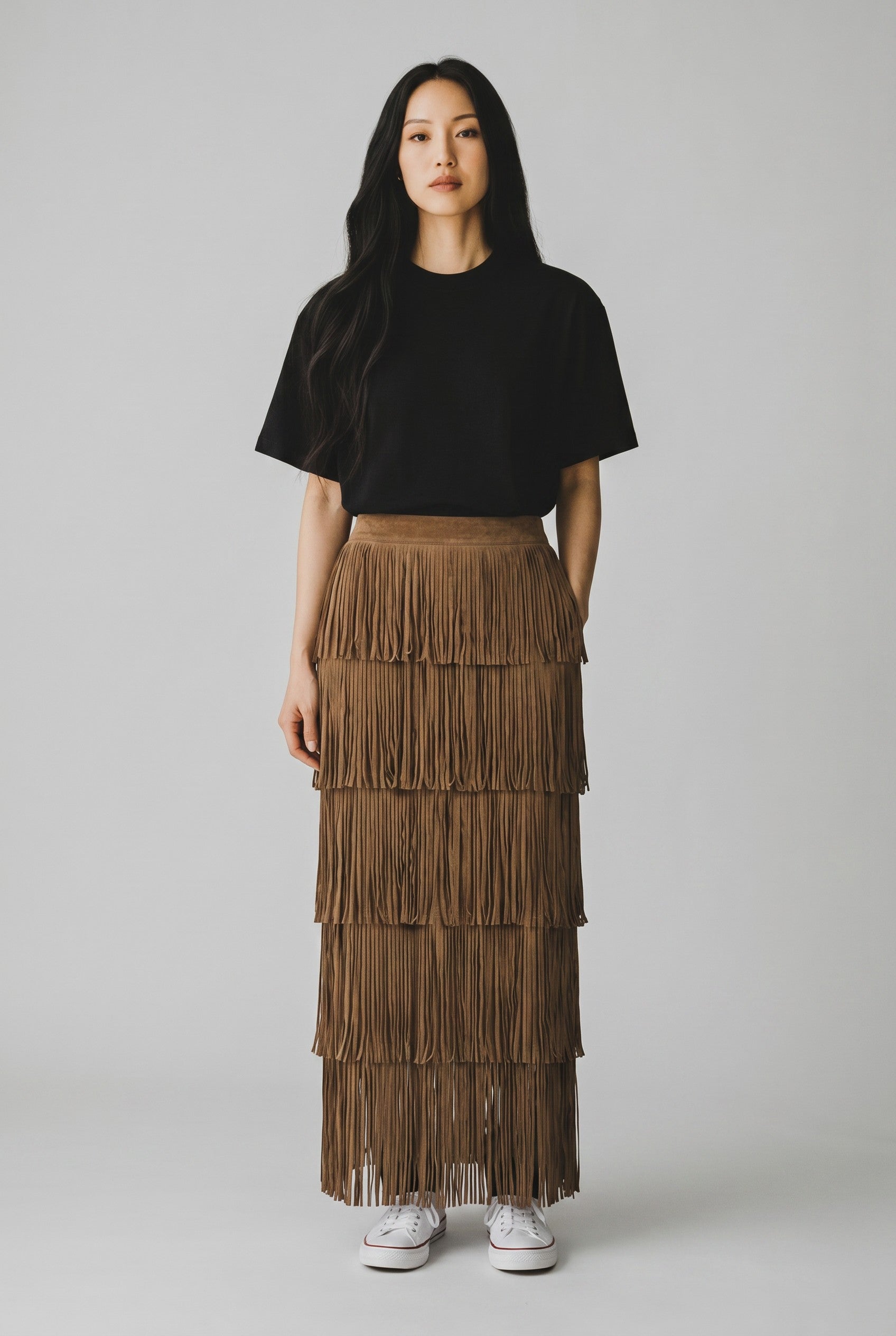 Model wearing a Color's Wholesale mink brown tiered suede fringe midi skirt with a black t-shirt and white sneakers.