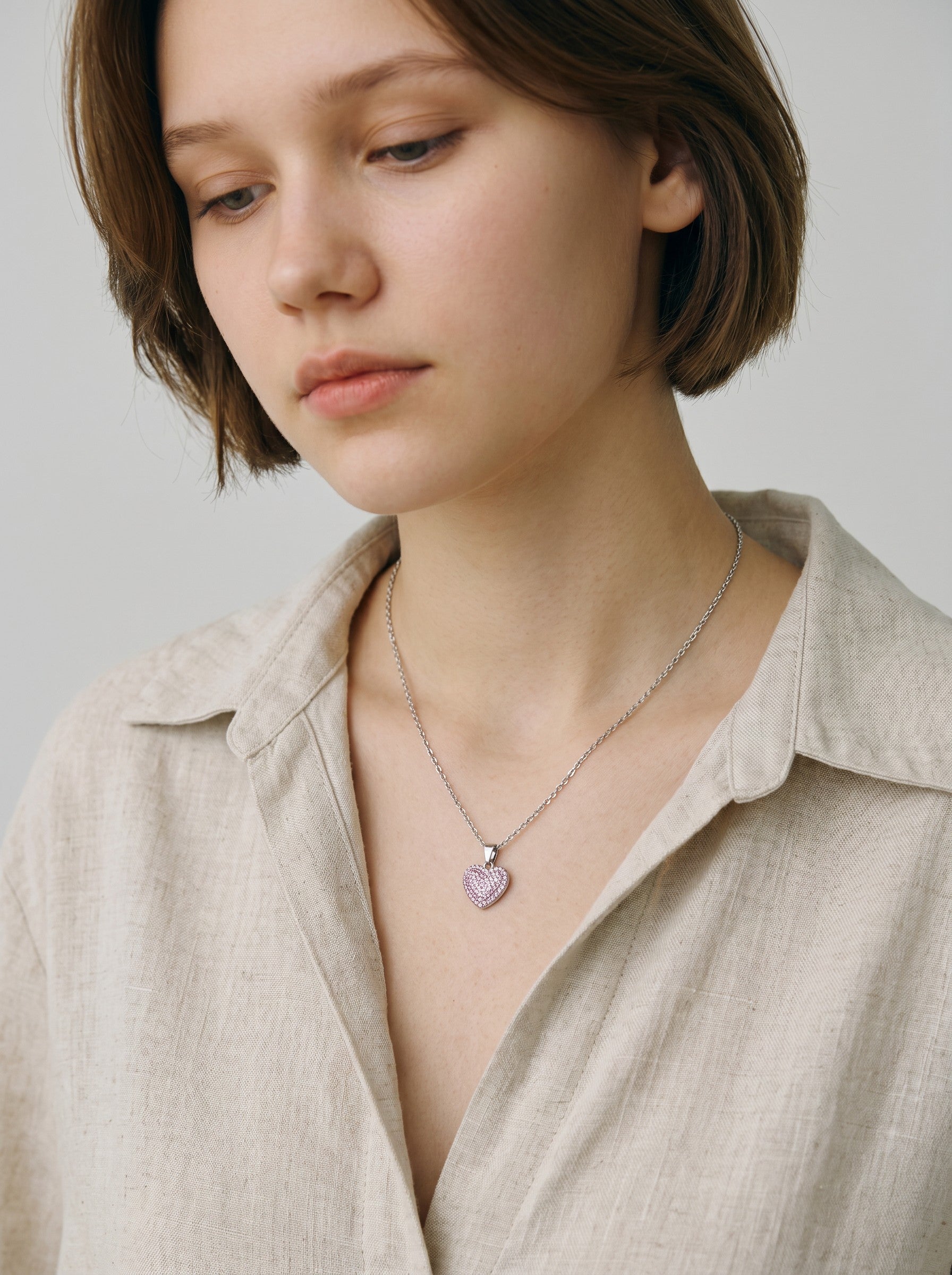 Color's Wholesale silver chain necklace featuring a small heart pendant with pink pavé crystals on a woman