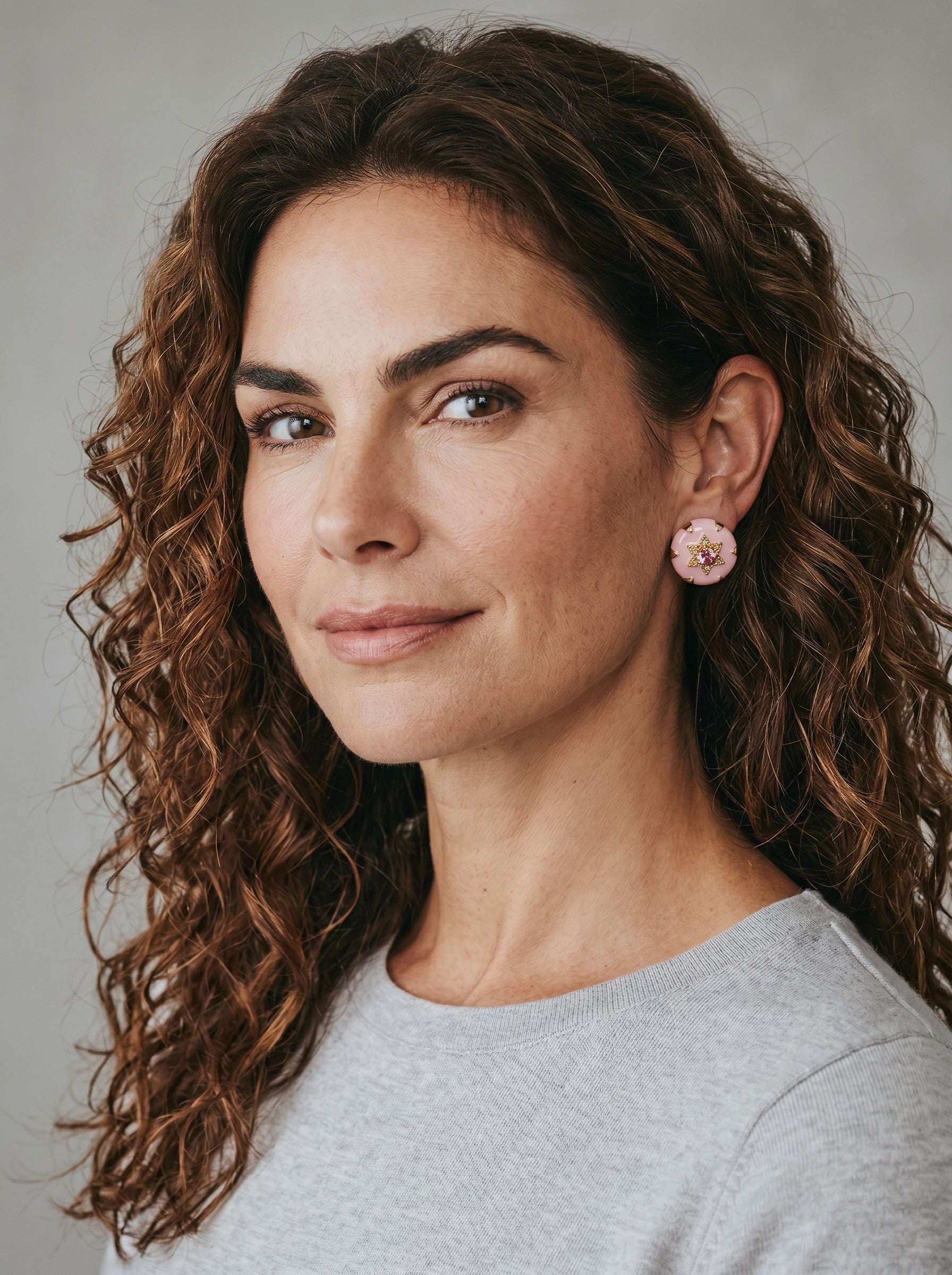 Woman wearing Color's Wholesale pink round stud earrings with a central gold star detail on a grey background