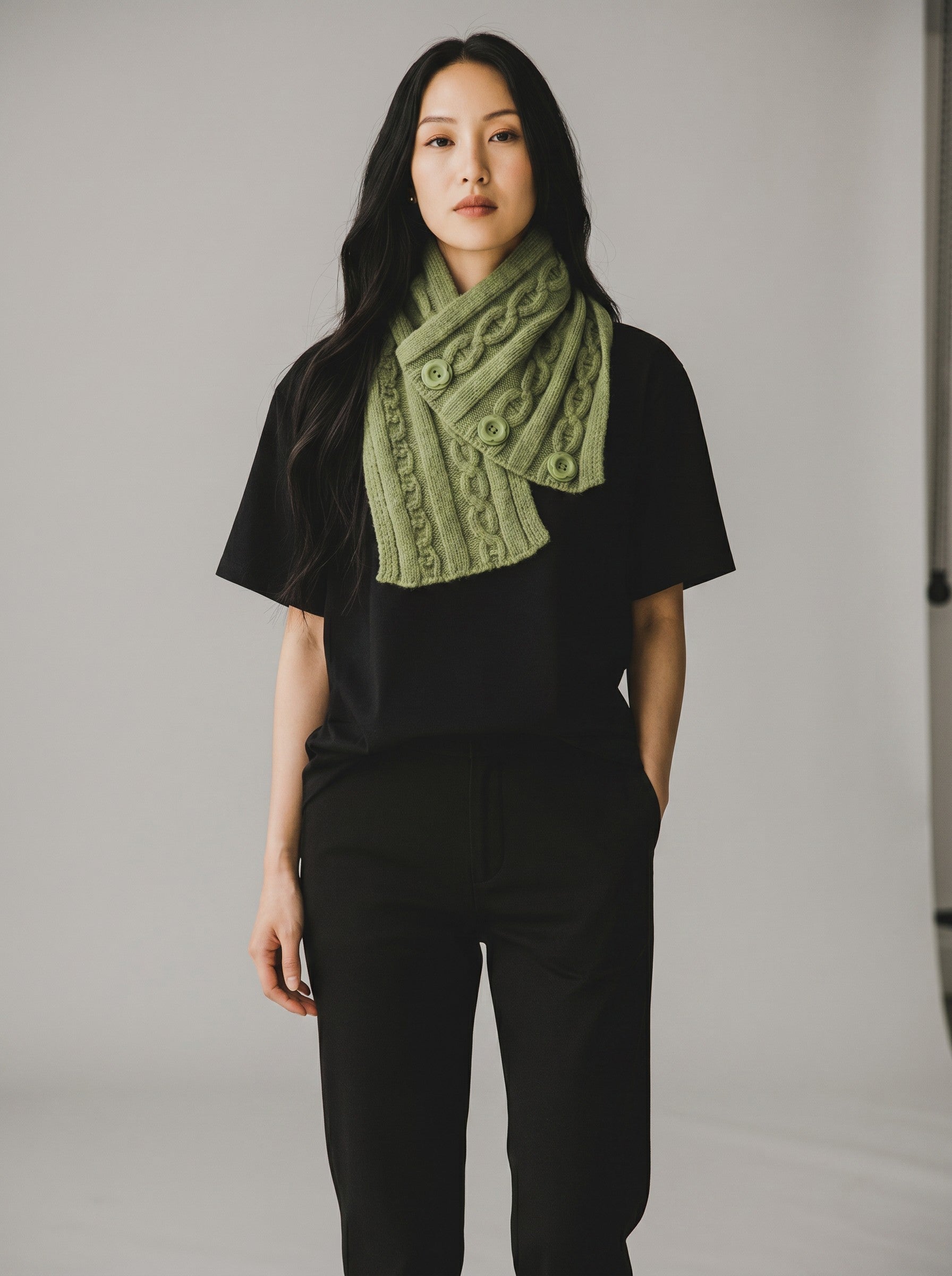 Color's Wholesale sage green cable knit scarf with button details worn by a model in a black t-shirt