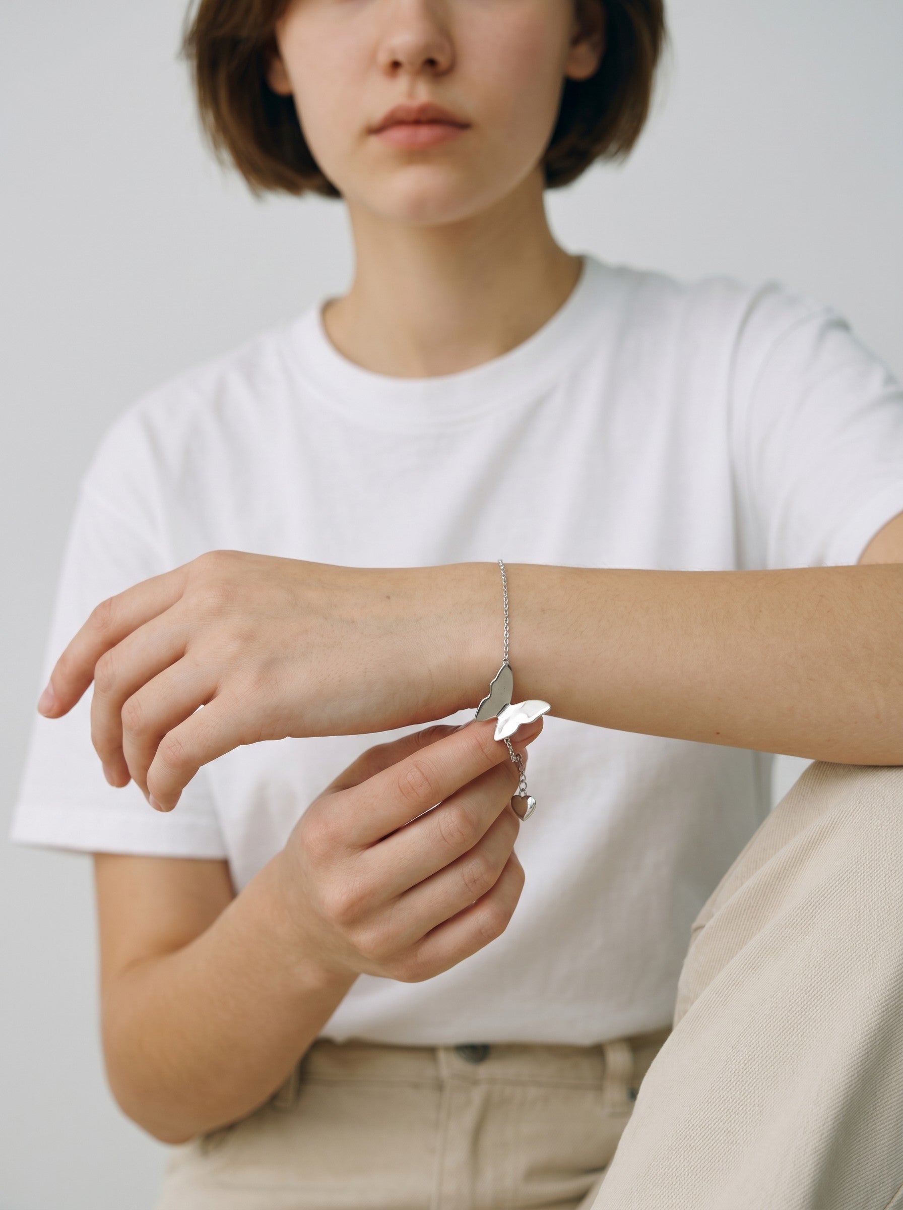 Color's Wholesale silver butterfly charm bracelet worn on a woman's wrist with a white t-shirt