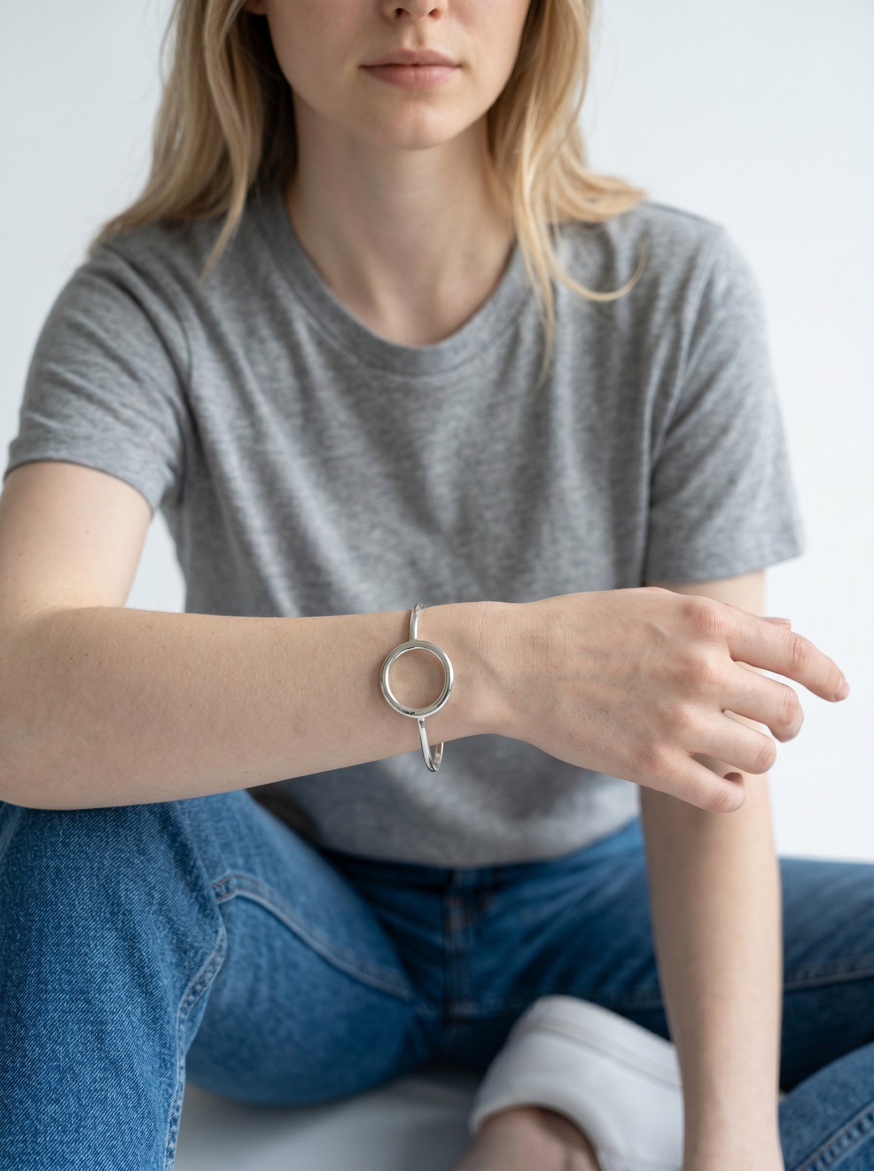 Color's Wholesale silver tone bangle bracelet with a circular pendant worn on a woman's wrist