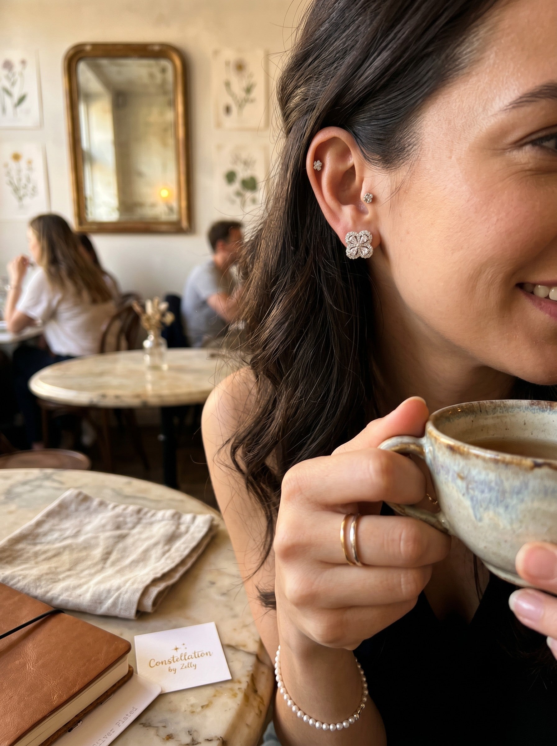 Color's Wholesale silver clover-shaped stud earrings with sparkling stones worn by a woman in a cafe