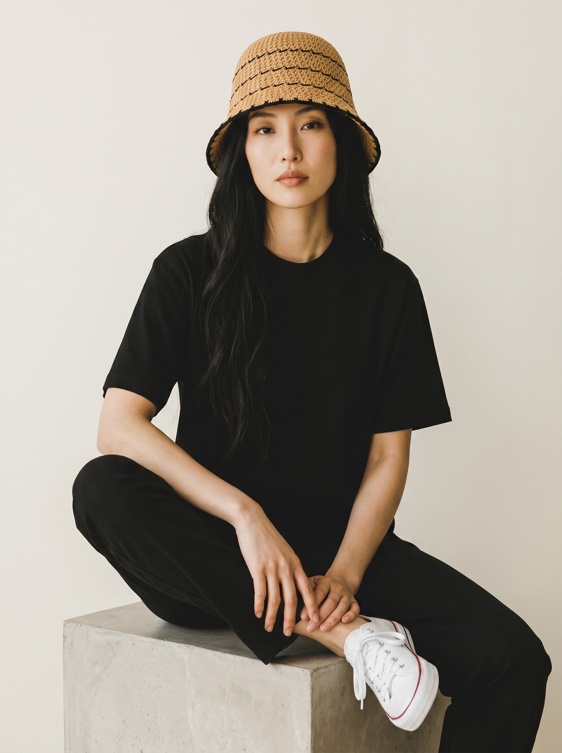 Color's Wholesale hand-crocheted straw bucket hat with black trim and horizontal stripes. Model wears black outfit.
