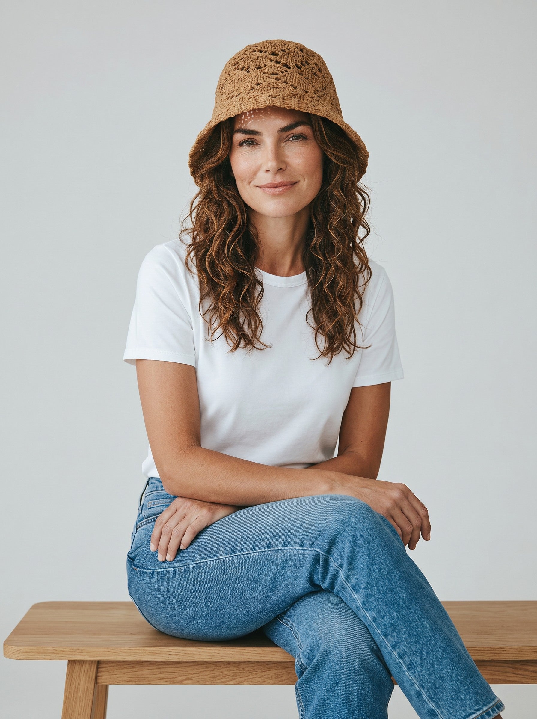 Color's Wholesale tan crocheted cotton bucket hat with open knit pattern and flower detail. Model wears white t-shirt and jeans.